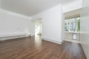 Home A contemporary empty apartment with white walls and wooden flooring, featuring large windows.
